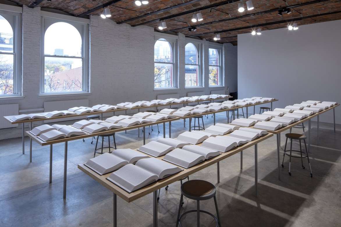 A room with three long tables with rows of open books.