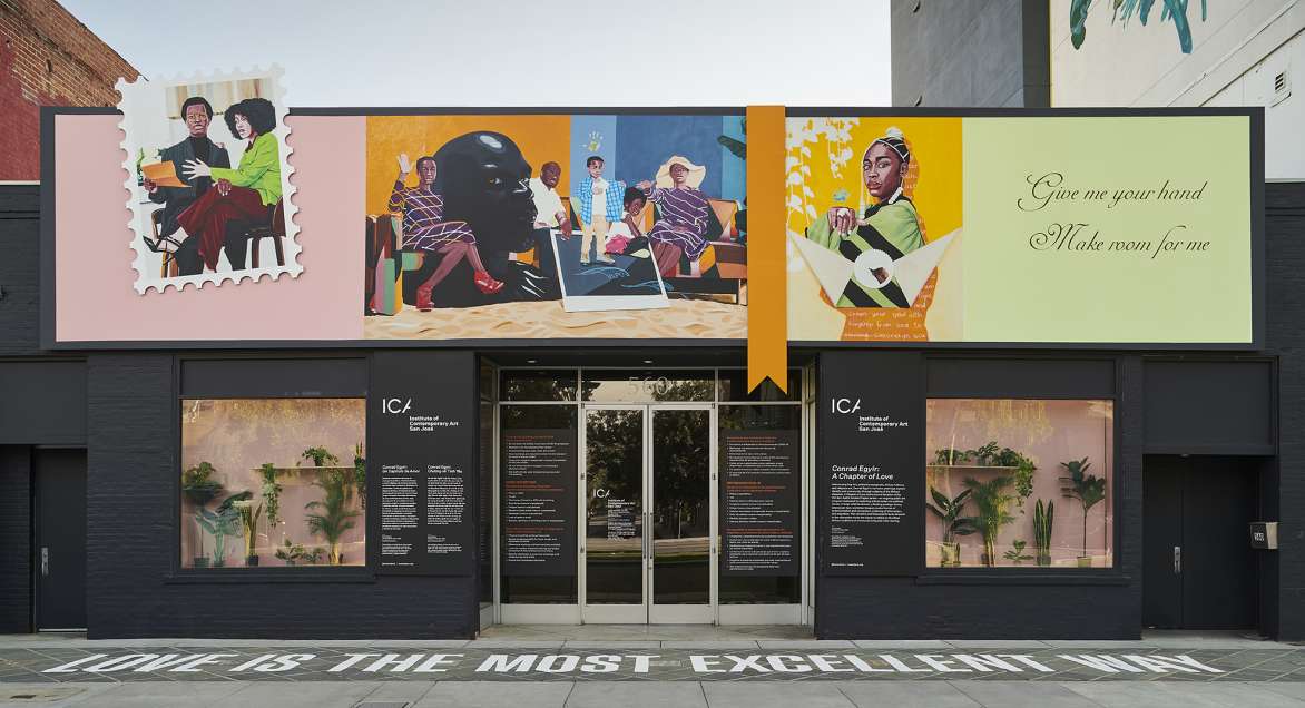 Image of the front of a building with large portraits of people hang on top of the facade. 
