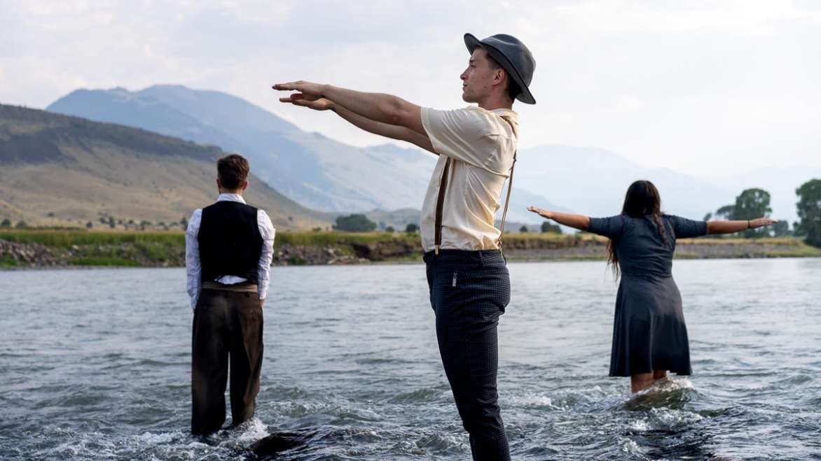 Three people standing in shallow water with mountains in the background.